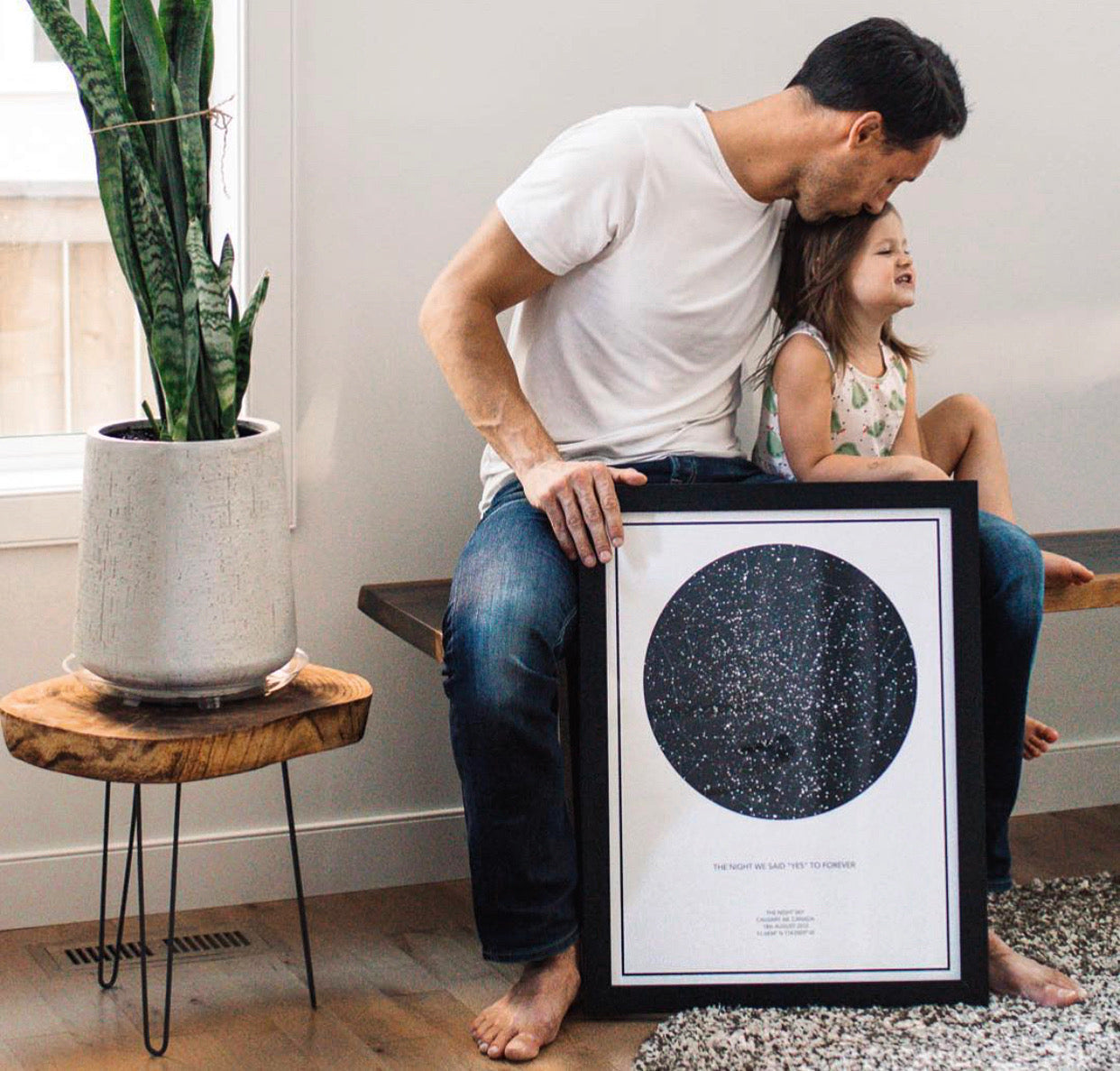 dad kissing his daughter while posing with his star map next to a plant