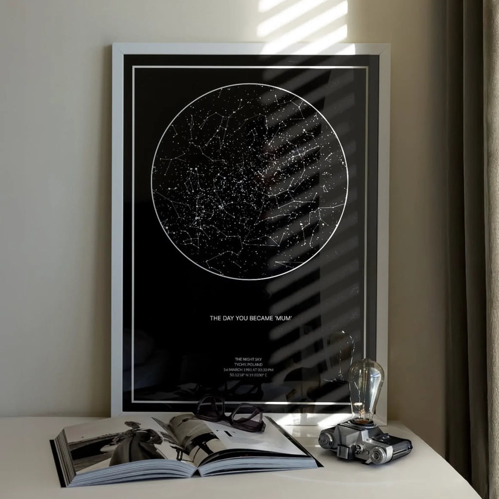 Framed personalized star map print on a tabletop with an open book and decor items