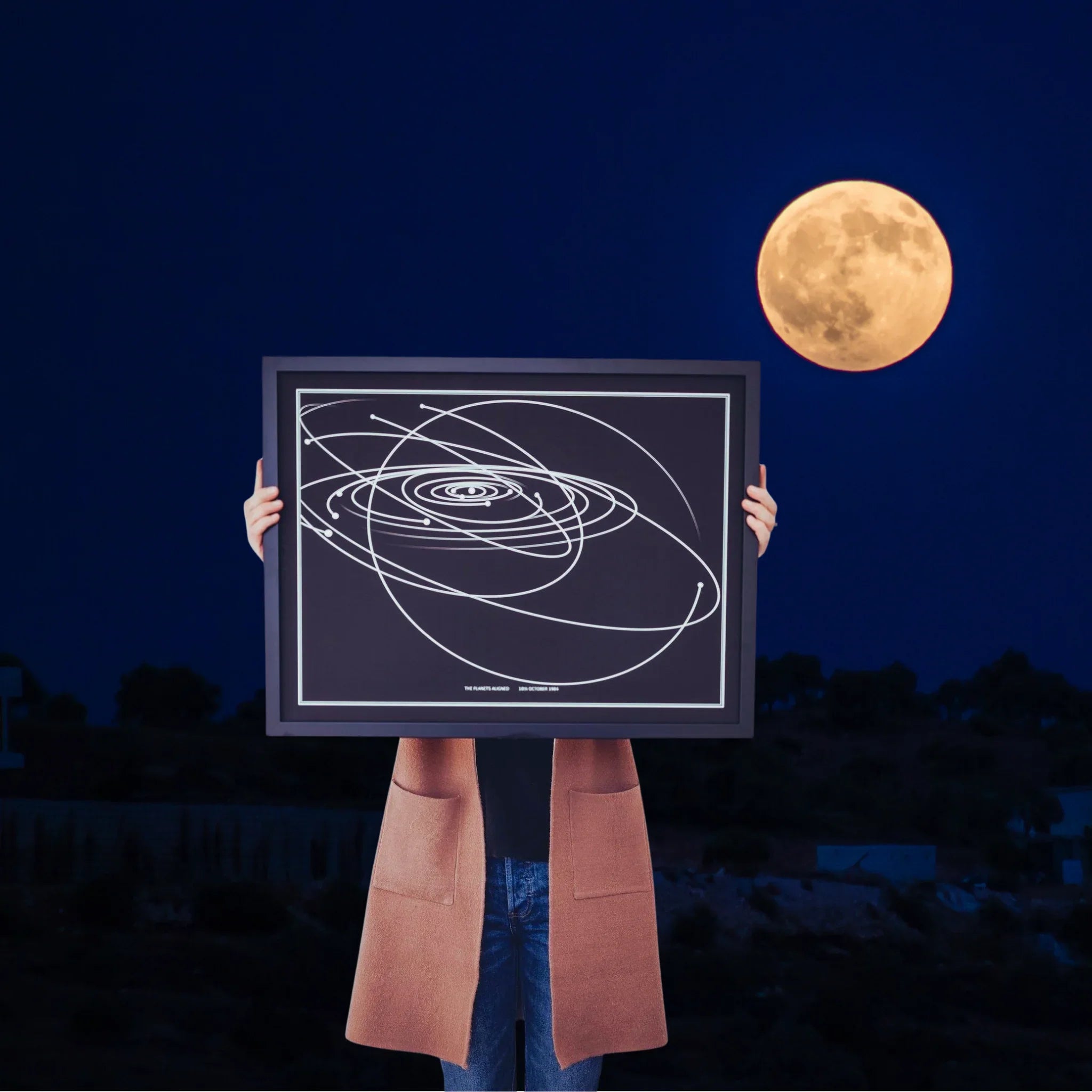 Person holding framed custom star map print at night with full moon in background