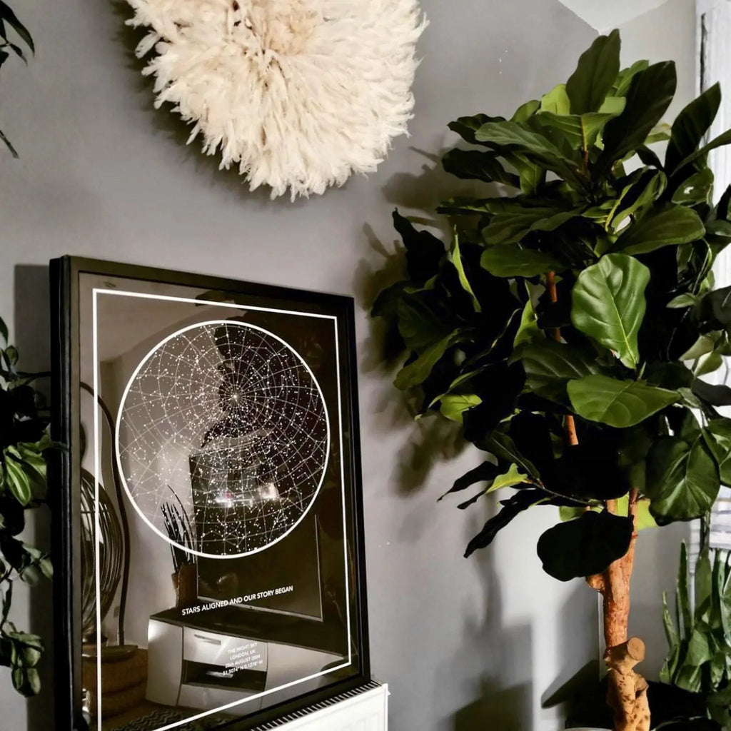 Framed personalized star map print on wall beside green houseplant in modern living room decor.